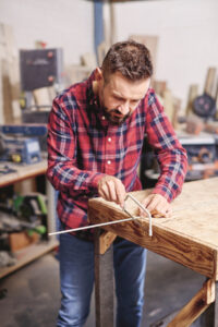 man holding a threaded rod at the edge of a wooden work bench and sawing&hellip;